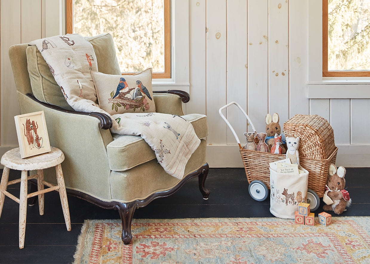 Nursery room corner with armchair, Coral and Tusk Alphabet Quilt, Bluebird Pocket Pillow, baby doll stroller and toys on the floor.