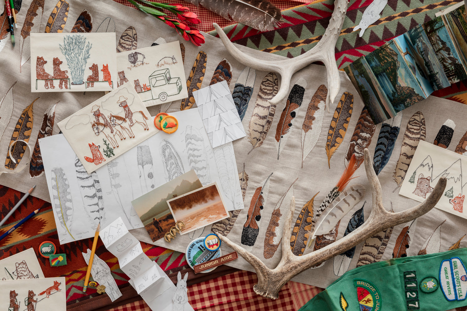 Flatlay of embroidered feather table runner, drawings and cards