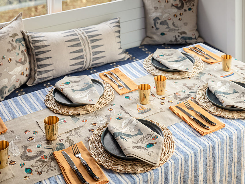Dining table set with Coral and Tusk embroidered coastal table runner and dinner napkins, striped table cloth and yellow accent napkins.