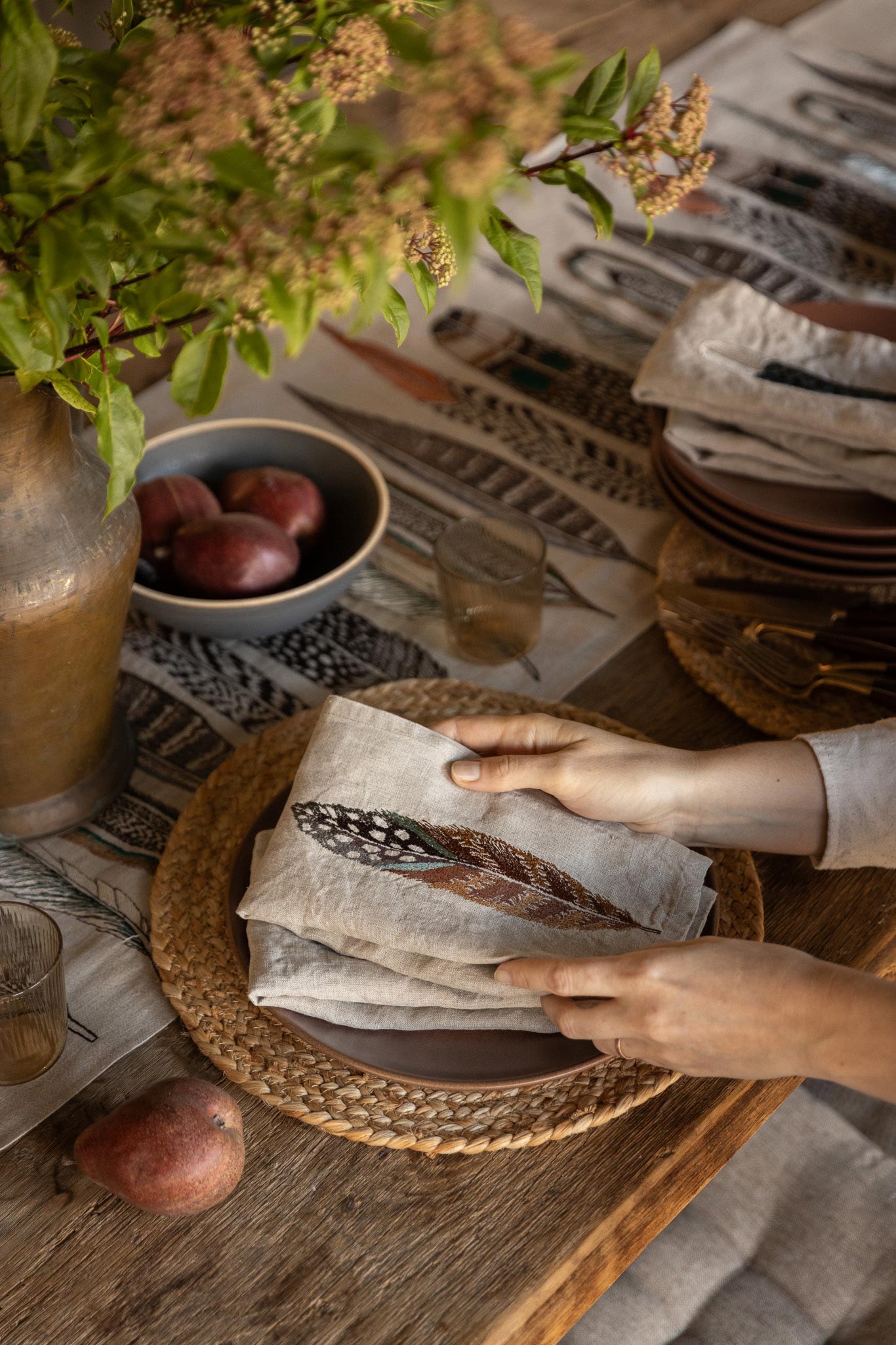 Embroidered Feathers Table Runner and Fowl Feather dinner napkins on a rustic wood table with wicker chargers and apples