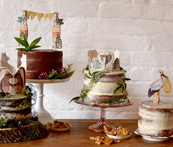 Image of four cakes on vintage cake stands decorated with flowers and Coral and Tusk cake toppers. 