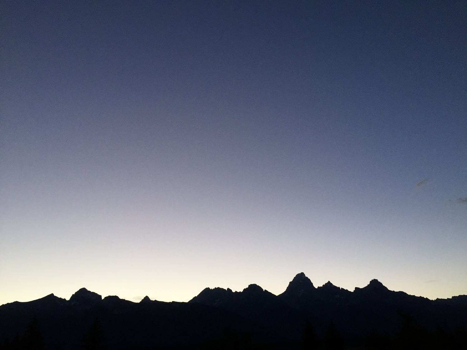 Landscape photo of Wyoming mountain range silhouette, sun has just set behind, dark blue night sky. 