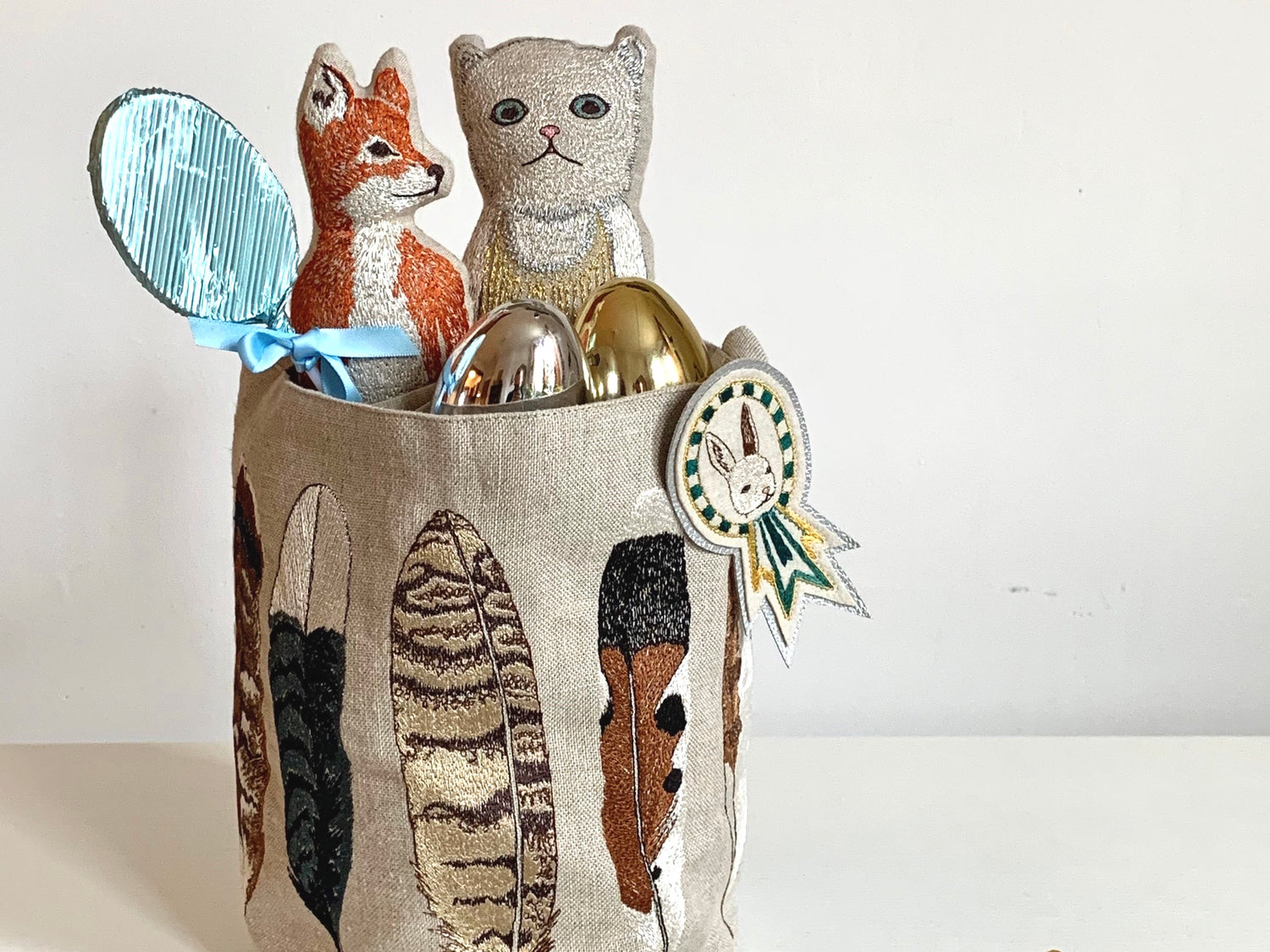 Embrodiered feather bucket holding Easter eggs and pocket dolls