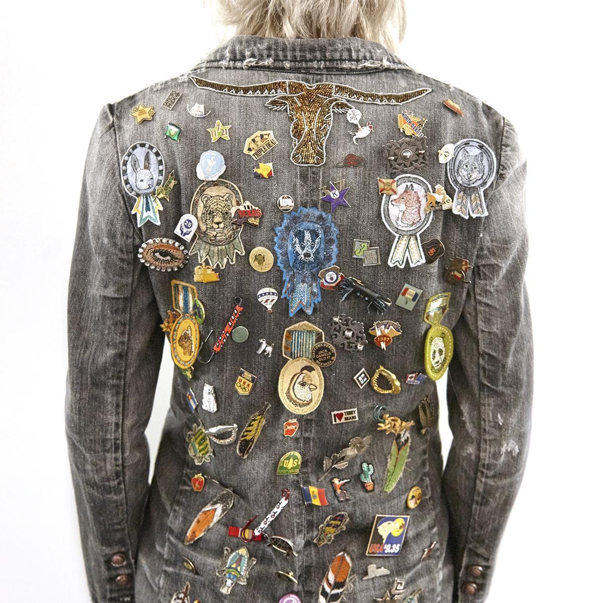 Back of a person wearing denim jacket covered in pins and patches, many from Coral and Tusk.
