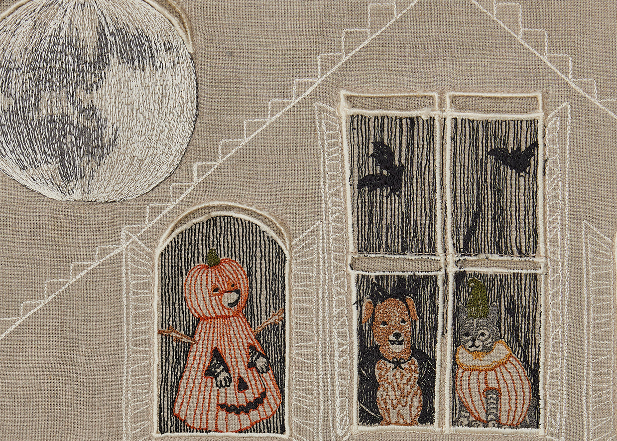 Detail of Coral and Tusk embroidered Halloween Advent Calendar, full moon over roof of house, Fox, Dog, and Kitty in costumes peeking out the windows.