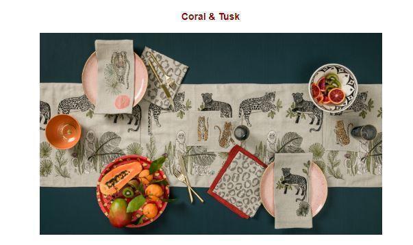 Image from Traditional Home Online featuring Coral and Tusk embroidered jungle motif table linens, overhead of table set with runner, dinner napkins, tea towels, bowl of fruit on dark green table cloth.