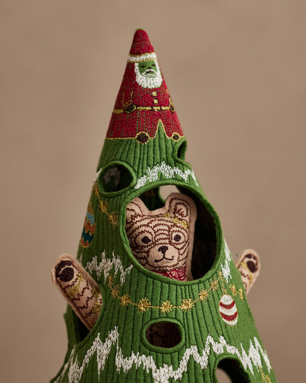 Close-up of the top half of the Coral & Tusk Christmas Tree Bear, showing the red Santa topper at the top and Bear's smiling face and tinsel-trimmed paws peeking through cut-outs.