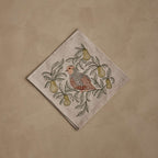 Coral & Tusk embroidered linen Partridge in a Pear Tree Dinner Napkin, folded, featuring a partridge perched among pear branches, leaves, and pears in earthy gray, rust, and olive tones.