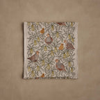 Coral & Tusk embroidered linen Partridge in a Pear Tree Table Runner, folded, featuring edge-to-edge stitched pear branches, leaves, and partridges with baby chicks in earthy tones of olive green, rust, gray, and gold.