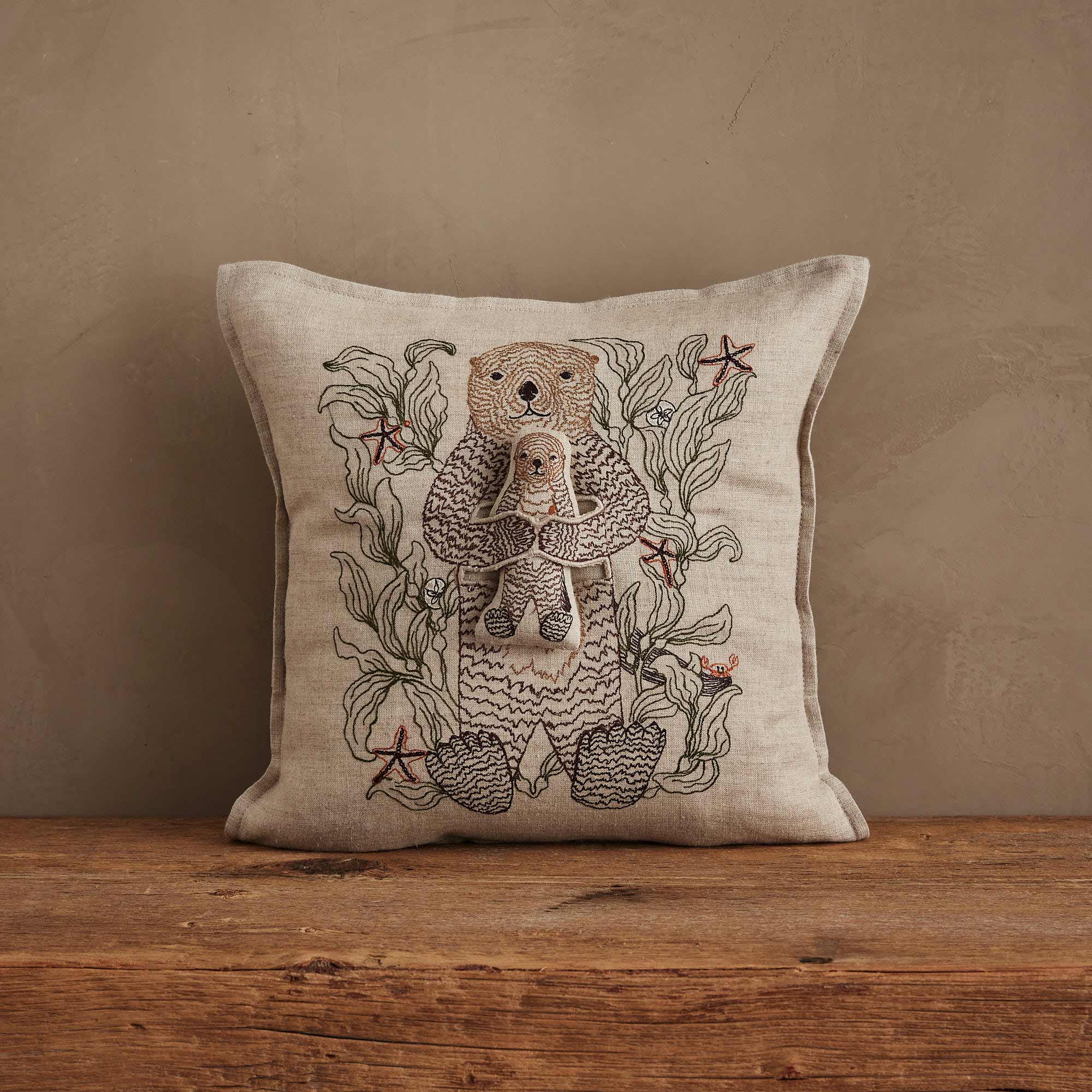Coral & Tusk Otter Mama Pocket Pillow, 12x12 inch natural linen pillow with intricate embroidery of a mama otter cradling a removable baby otter pal among kelp and starfish.