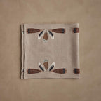 Coral & Tusk linen Turkey Feather Border Table Runner, folded, featuring detailed embroidery of feathers from birds including turkey, mallard, and wood duck patterned along the edges.