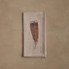 Coral & Tusk folded linen napkin featuring an embroidered brown Turkey feather with a stitched blue tip.