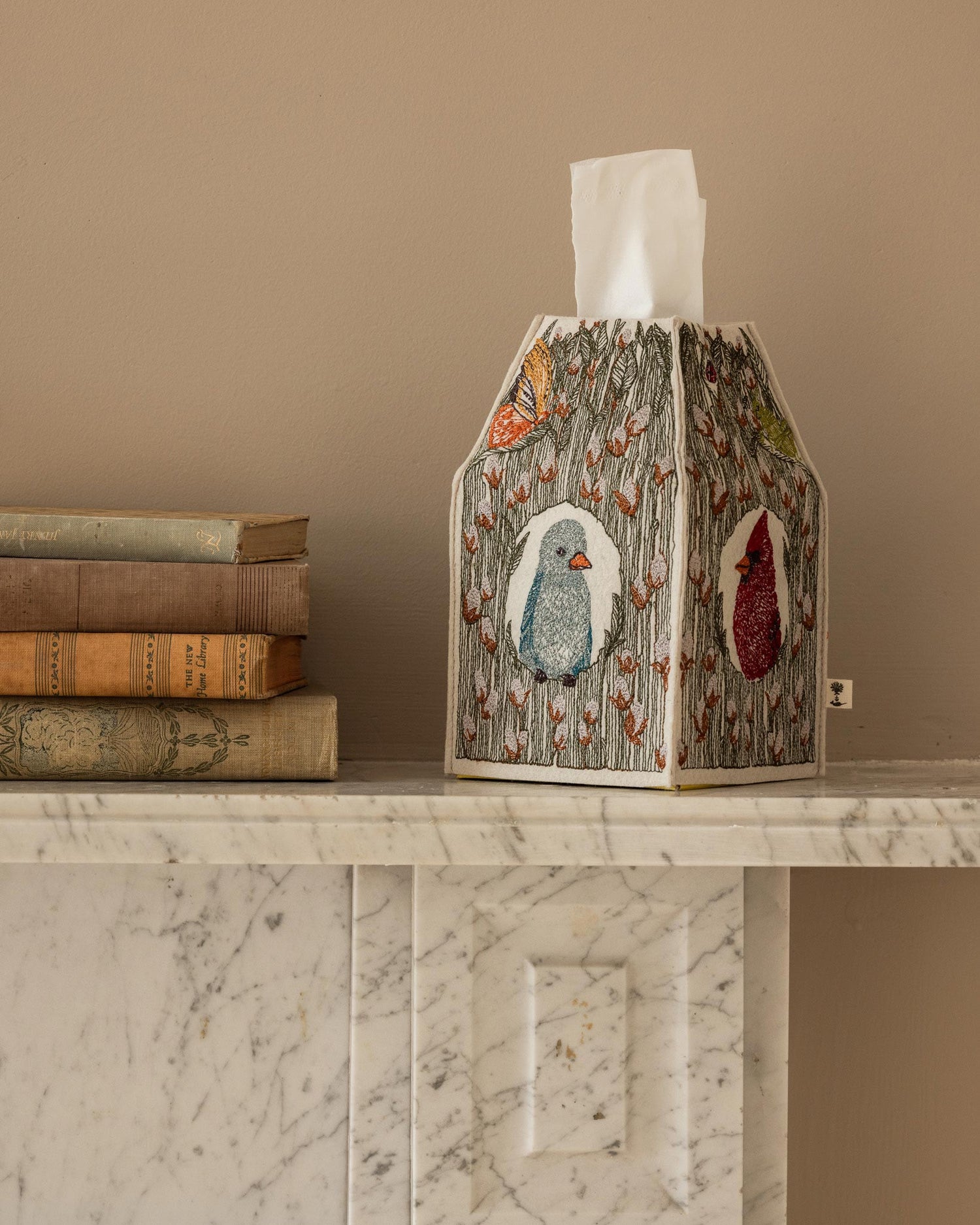 Coral & Tusk Birdhouse Tissue Box Cover embroidered decorative cover styled on a marble mantle with books.