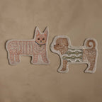 Two Coral & Tusk embroidered linen pet-shaped pouches, Dog in Sweater Pouch and Orange Kitty Pouch, facing each other, displayed on a textured beige background.