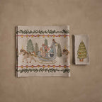 Coral & Tusk Jingle Bells Table Linens Set, folded and displayed flat, showing the Jingle Bells Table Runner embroidered with a sleigh and horse scene framed by pine garland and bells, beside four stacked folded Peek a Tree Dinner Napkins with an embroidered Christmas tree design.