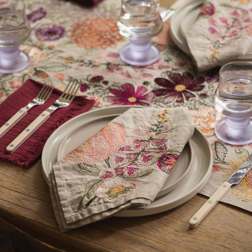 Coral & Tusk embroidered Paradise Garden Table Runner and Blush Bouquet Dinner Napkin, styled with cutlery and glasses on a wooden table.