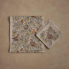Coral & Tusk Partridge in a Pear Tree Table Linens Set, folded and displayed flat, showing the Table Runner in an all-over pattern of pear branches and partridges with baby chicks, beside a stack of matching Dinner Napkins each with a single embroidered partridge.
