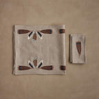 Coral & Tusk Turkey Feather Table Linens Set, folded, showing the Turkey Feather Border Table Runner with embroidered brown, black, and white turkey, mallard, and wood duck feathers, beside a stack of Turkey Feather Dinner Napkins, each with a single embroidered turkey feather.