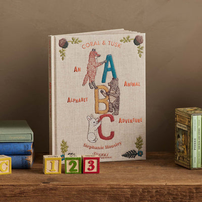 Coral & Tusk children's book titled 'ABC: An Animal Alphabet Adventure' by Stephanie Housley on a wooden shelf with colorful blocks.