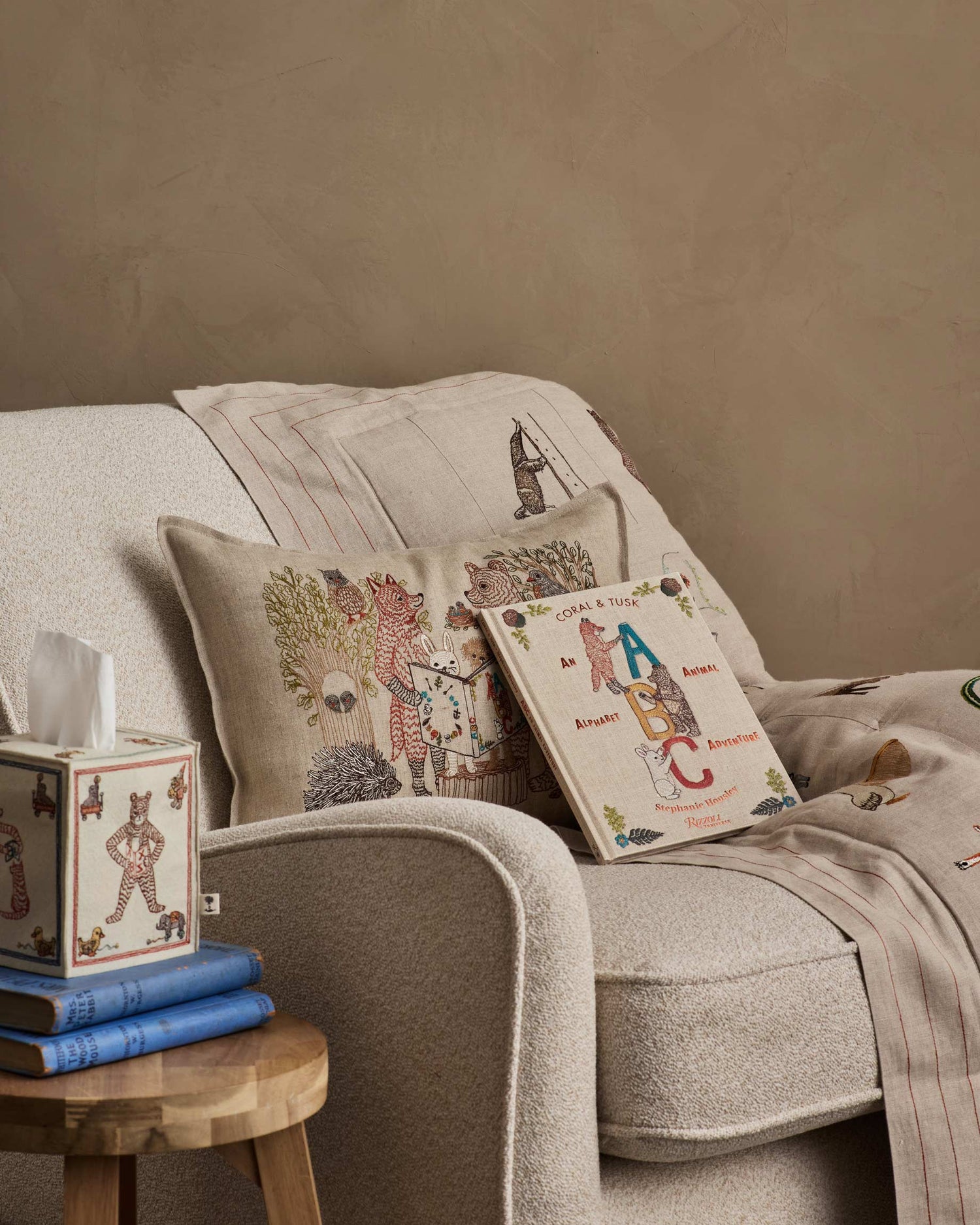 Chair styled with a Coral & Tusk decorative Storytime Pillow, ABC Book, and Alphabet Quilt, accompanied by a small wooden table holding a Coral & Tusk ABC Tissue Box Cover and books.