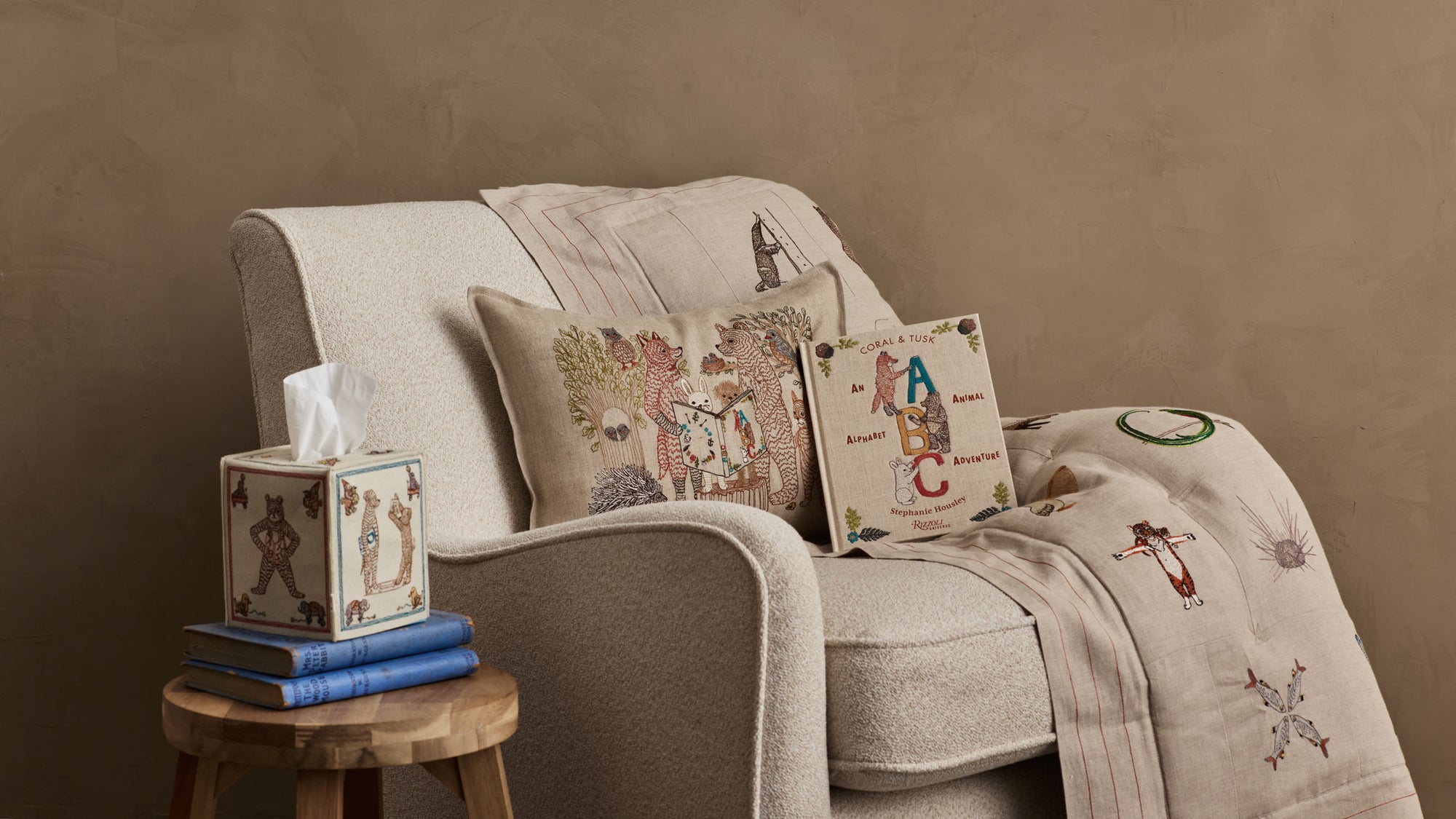Chair styled with a Coral & Tusk decorative Storytime Pillow, ABC Book, and Alphabet Quilt, accompanied by a small wooden table holding a Coral & Tusk ABC Tissue Box Cover and books.