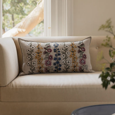 Coral & Tusk Spring Stems decorative pillow featuring an embroidered floral design on a white sofa by a sunlit window.
