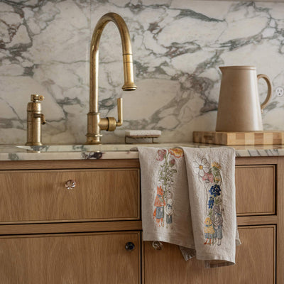 Kitchen sink with gold faucet and marble backsplash, styled with two Coral & Tusk embroidered linen tea towels featuring spring animal motifs.